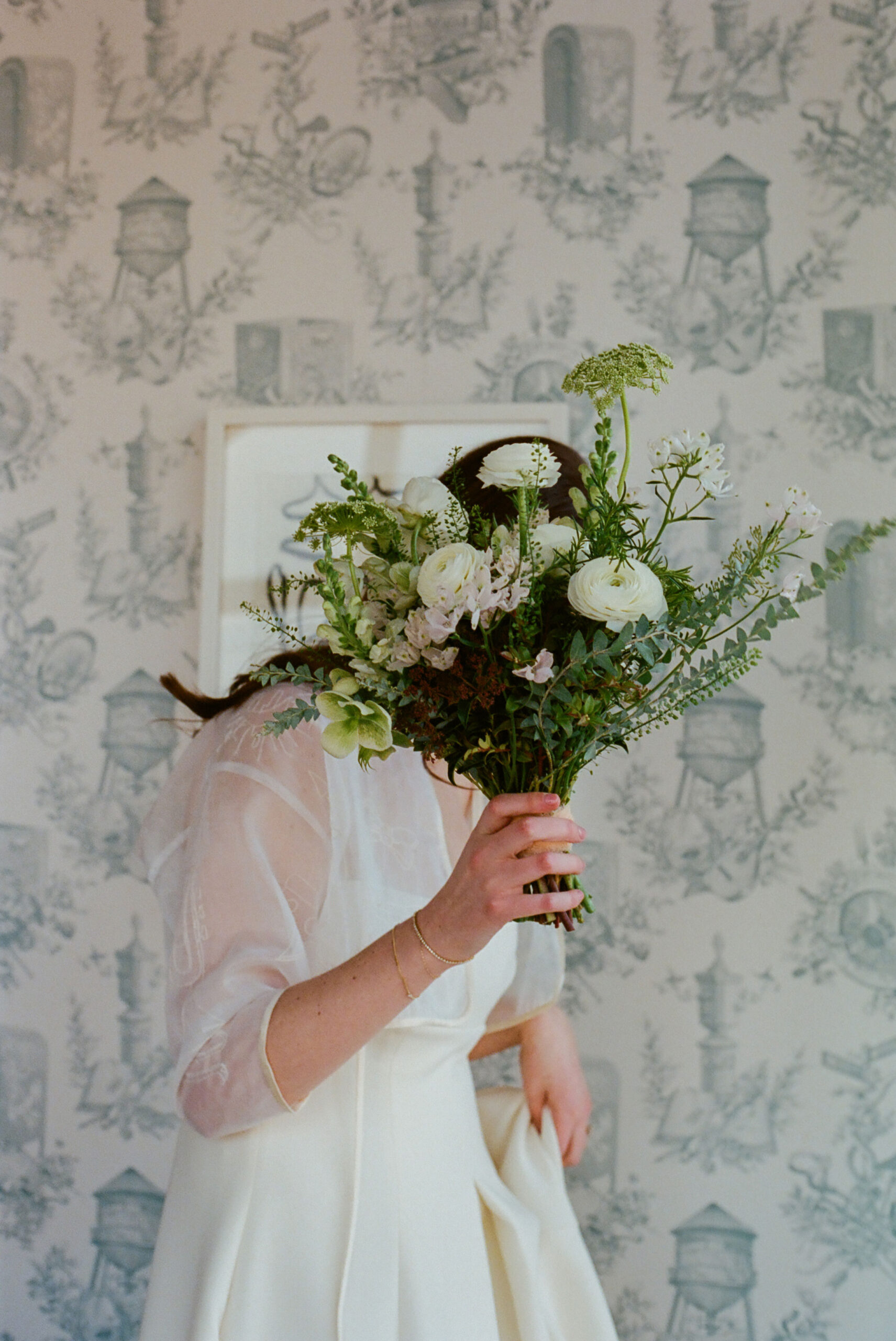 green floral arrangement in front of brides face emilia wickstead wedding dress shot on film by parkers pictures